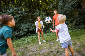 Family of four playing soccer in the park.