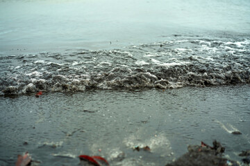 Black foamy waves from the sea to the sandy beach, sea water pollution background, view from the beach. Rubbish disposal and trash management, Environmental pollution concept.