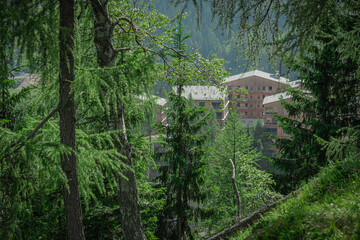 Fototapeta premium Modern buildings with fancy wooden facade in high alpine village of Nassfeld, austria. Cloudy summer day, looking through trees