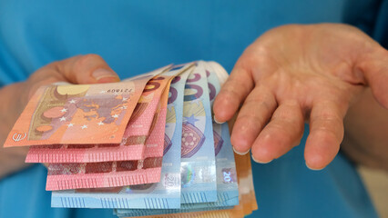 A close-up shot of the hands of a nurse in a turquoise uniform, with money in one hand and the empty open palm of the other hand. The concept of decent remuneration for medical and aged care staff.