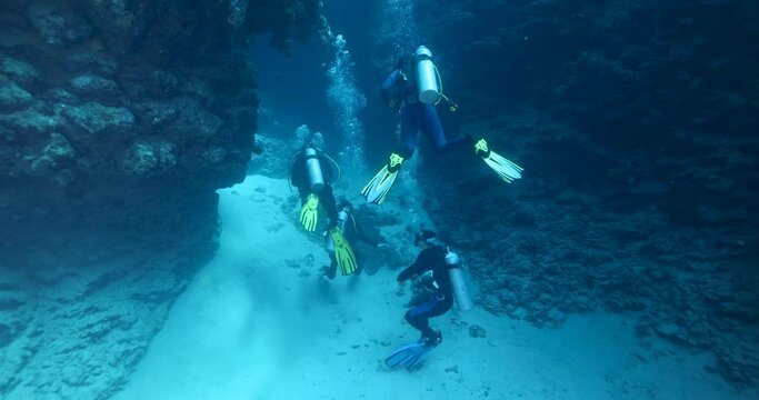 Group of divers swimming in an underwater cave canyon. Diving instructor and group students in underwater exploration. The instructor teaches the students. Scuba diving training and education.