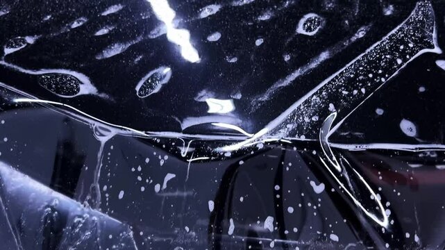 Employees of a car detailing studio apply clear protective PPF film on the hood of a black car. The video showcases the meticulous process ensuring high-quality protection and finish.