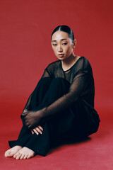 Fashion asian woman sitting with crossed legs and hands on knees against red background