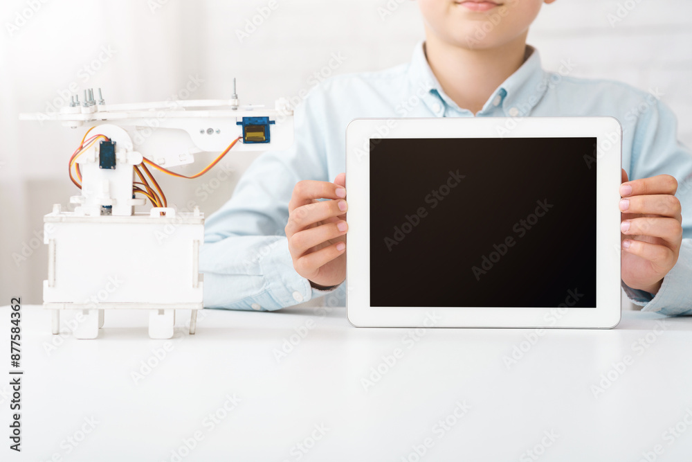 Poster a young person is holding a tablet with a blank black screen in front of a small robot on a white ta