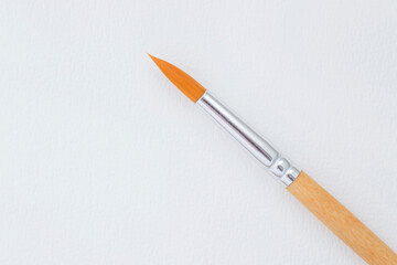 wooden paint brush laying on blank sheet of watercolor paper