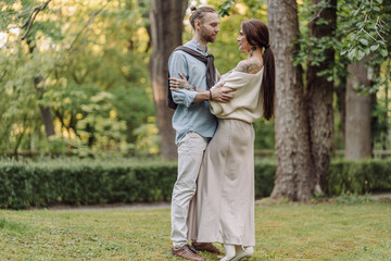 Love, hug and happy with couple in park for romance, bonding and summer vacation. Loving young couple hugging and smiling together on nature background. Beautiful girl with tattooed body outdoor.