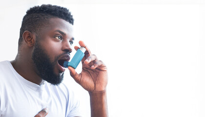 An image of African American man using an inhaler to treat his asthma. He is holding the inhaler in...