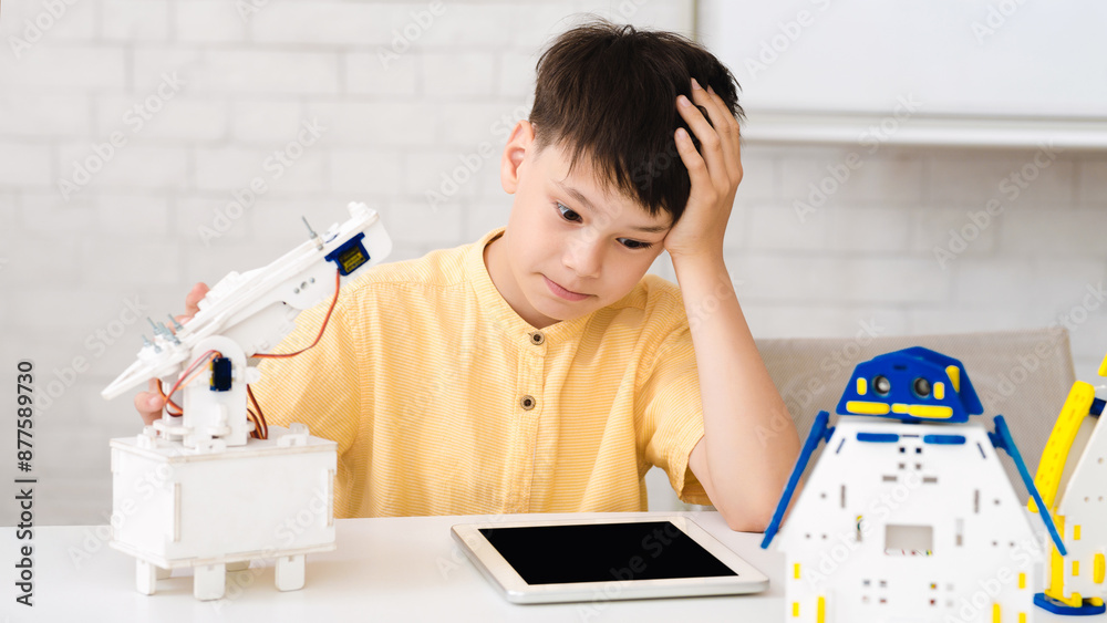Aufkleber a young boy sits at a table, looking frustrated as he works on a robotics project. he has his hand o