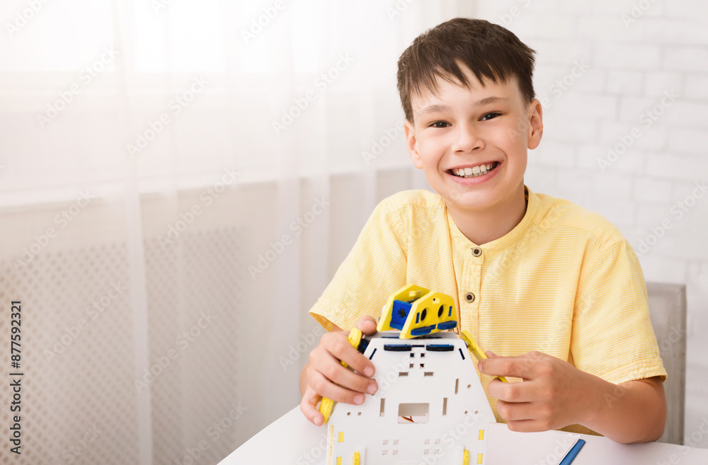 Poster a young boy with short brown hair sits at a table while building a toy robot, his face is lit up wit