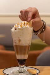 Latte Macchiato is a coffee drink made of layers of milk and espresso, The woman grabs a cookie from her coffee with her hand, the woman's hand facing the coffee