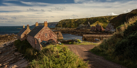 Small harbour in the village of Cove, east coast of Scotland, with two fishermen houses and a stone dock. Surrounded by grassy cliffs