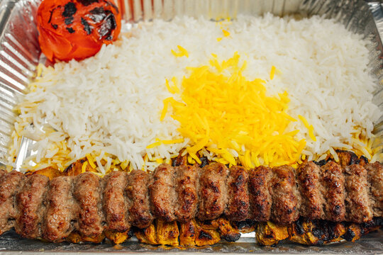 takeout platter of Persian food: basmati rice sprinkled with saffron rice, koobideh kabob, grilled whole tomato