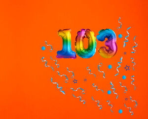 Multicolor balloon number 103 - Confetti explosion on orange background. Birthday card