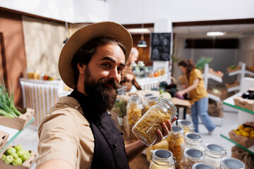 Zero waste shop entrepreneur using selfie camera on smartphone to promote environmentally conscious vegan products online. Ecofriendly supermarket owner making social media content for followers