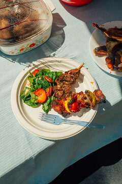 grilled meat and vegetable kabob skewers on paper plate with serving of spinach and strawberry salad