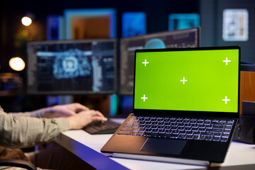 Green screen laptop next to man updating artificial intelligence neural networks, writing binary code script. IT professional upgrading high tech AI, mockup notebook on desk, close up