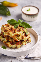 Zucchini Waffles with garlic, cheese and herbs, served with basil leaves and sour cream sauce. Healthy food.