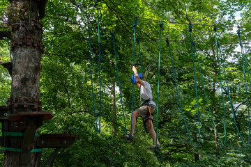 Boy in helmet doing rope course on tree in forest with focused expression on sunny day. Concept of adventure, outdoor activities, and physical fitness. High quality photo
