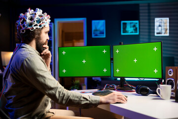 Man with EEG headset programs brain transfer into multimonitor setup green screen computer, merging...