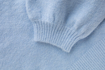 Pastel blue sweater sleeve with cuff as background. Knitted wool handmade sweater. Warm and fashionable clothes. Comfortable style cloth. Cozy composition. Soft focus