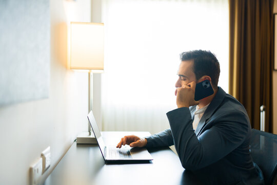 Busy businessman is juggling tasks, working on a laptop and taking a call in his hotel room
