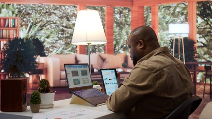 Entrepreneur reviews business updates and details at his home, allocating resources and finishing operations tasks to achieve strategic goals, money management remote work. Camera B.