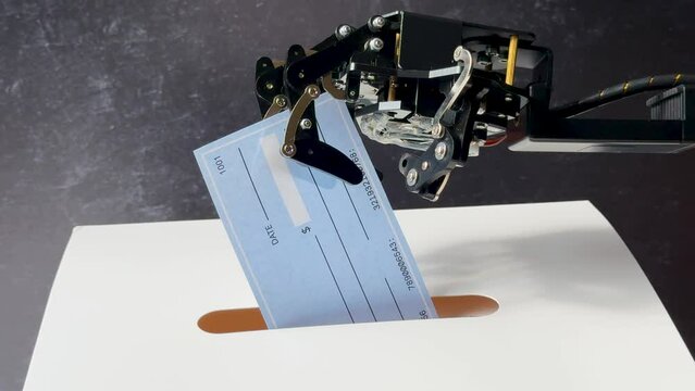 A robotic arm holds a blank check, placing it into a slot on a white surface with a dark background.
