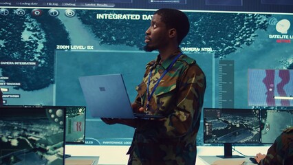 Military sergeant targeting enemy vessels on a gps satellite world map, operating from army power base monitoring room. Officer studies defense tactics on a tablet, command center. Camera B.