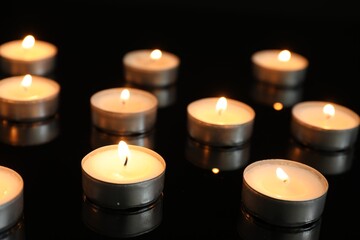 Many burning tealight candles on mirror surface against black background