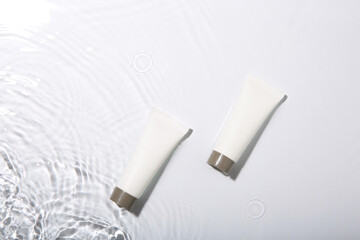 Cosmetic products. Tubes with cream in water on light background, top view