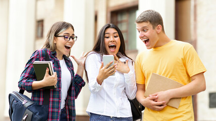Surprised students checking exam results on smartphone, resting in campus