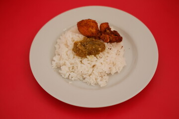 Rice with fried chicken and sambal in a white plate on a red background