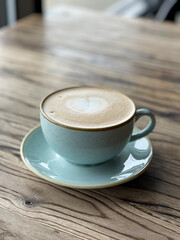 Cappuccino in a teal cup decorated with a heart on top on a wooden table