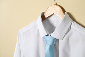 Hanger with shirt and necktie on beige background