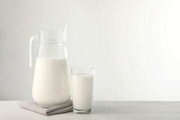 Jug and glass with fresh milk on light wooden table. Space for text
