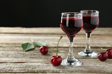 Glasses of delicious cherry liqueur on wooden table against dark background, space for text