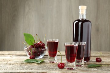 Bottle and shot glasses of delicious cherry liqueur with juicy berries on wooden table, space for text
