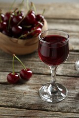 Delicious cherry liqueur in glass and fresh berries on wooden table