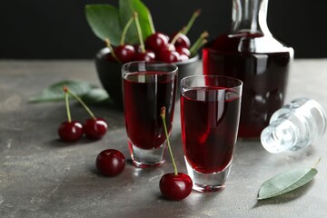 Delicious cherry liqueur in shot glasses, decanter and fresh berries on grey table