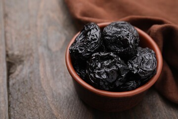 Tasty dried plums (prunes) in bowl on wooden table, closeup. Space for text