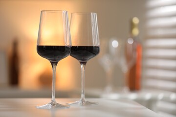 Red wine in glasses on white table against blurred background, space for text