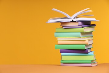 Stack of colorful books on orange background, space for text