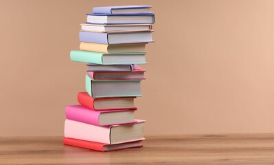 Stack of colorful books on wooden table against light brown background, space for text