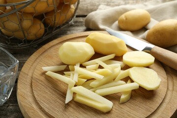 Whole and cut fresh raw potatoes near knife on wooden table