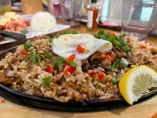 Cast iron plate of fried rice with fried egg on top and side of lemon