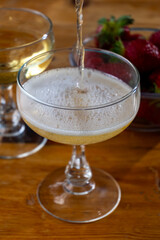 Pouring of brut champagne bubbles wine in coupe glasses and small bowl with fresh strawberries