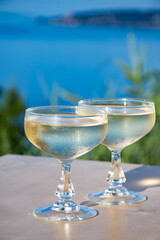 Sparkling wine, cava or champagne in two coupe glasses on table with view on blue sea, Menton and Monte-Carlo, French Riviera, France is summer