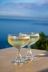 Cold sparkling wine, cava or champagne in two coupe glasses on table with blue sea water view