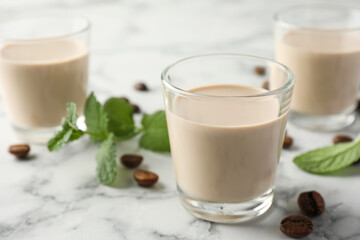 Coffee cream liqueur in glasses, mint and beans on white marble table, closeup