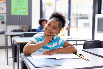 Portrait of happy african american schoolgirl sitting at desk in school classroom